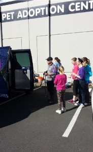 A group of people, including several children, stand outside next to a van in front of a building labeled PET ADOPTION CENTER. One person appears to be holding a leash or pet-related item.