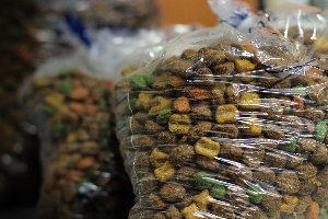 Clear plastic bags filled with multicolored dry pet food or kibble, including brown, green, and orange pieces, stacked closely together.