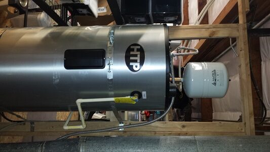 A large HTP-branded water heater tank with attached pipes and an expansion tank is installed vertically in a basement or utility room with wooden framing and exposed beams.